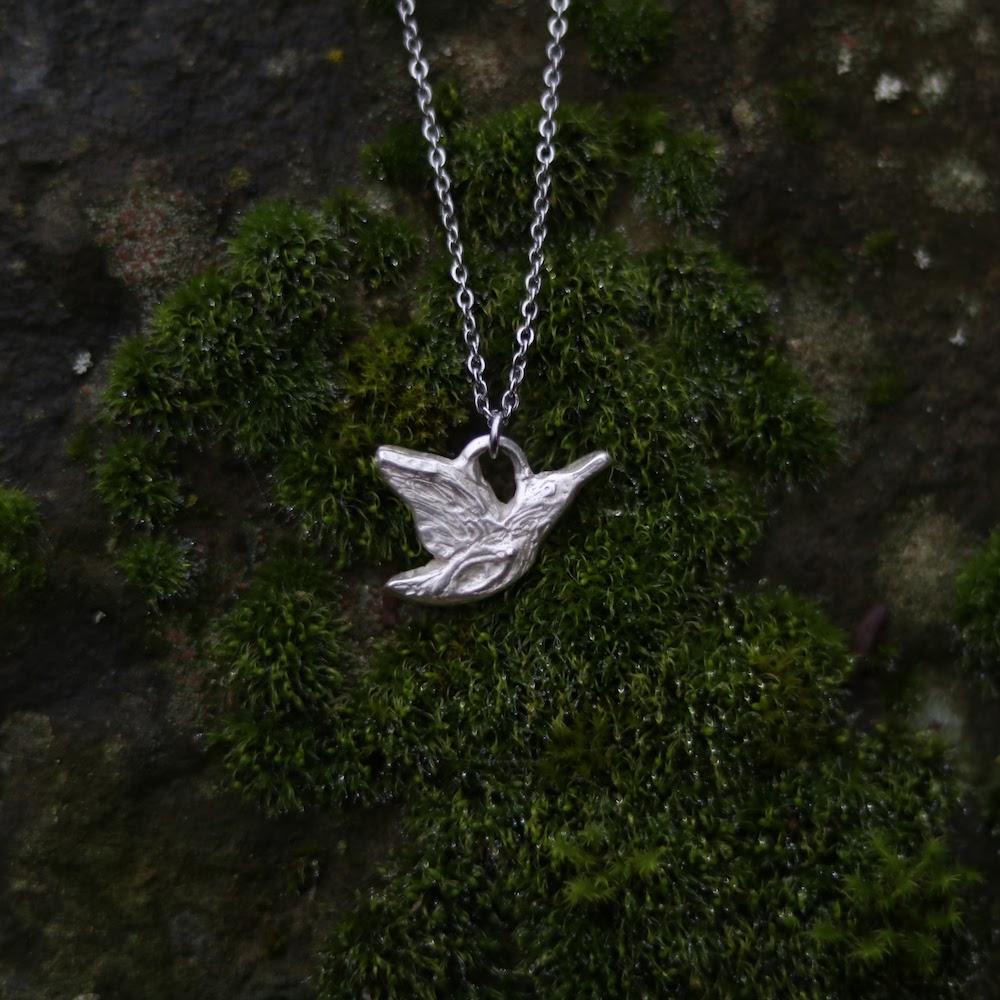 A sterling silver necklace featuring a queenfisher in determined flight. The bird's intricate design includes a subtle vulva on her breast, and textured wings.